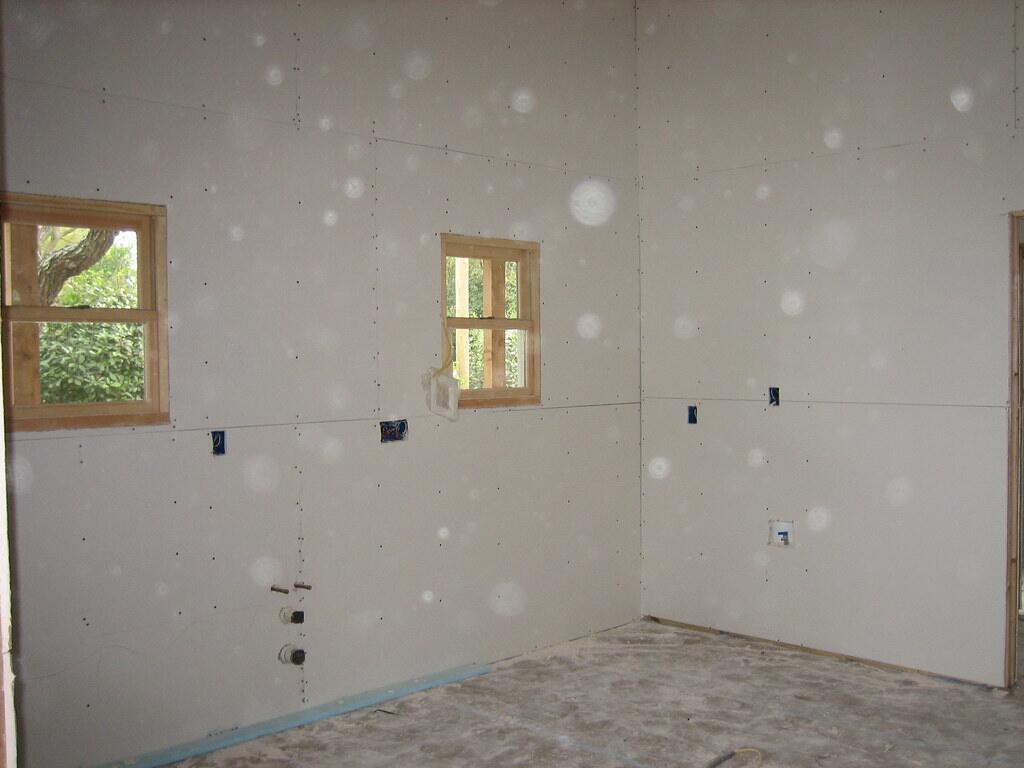Kamer met nieuwe gipsplaten tegen de muren, nog zonder naden en verf, met twee ramen