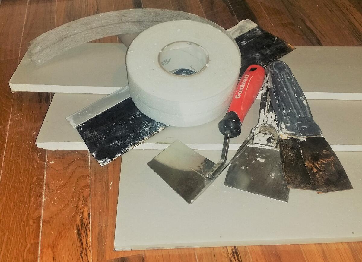 Stukken gipsplaat met een rol voegband en plamuurmessen op een houten vloer